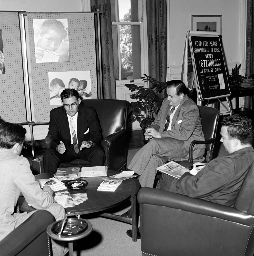 Director of Food for Peace, Richard Reuter (center-right), meets with Food for Peace staff in the Executive Office Building, Washington, D.C. June 29, 1963. Image source: Cecil Stoughton. White House Photographs. John F. Kennedy Presidential Library and Museum, Boston. JFKWHP-ST-328-1-63.